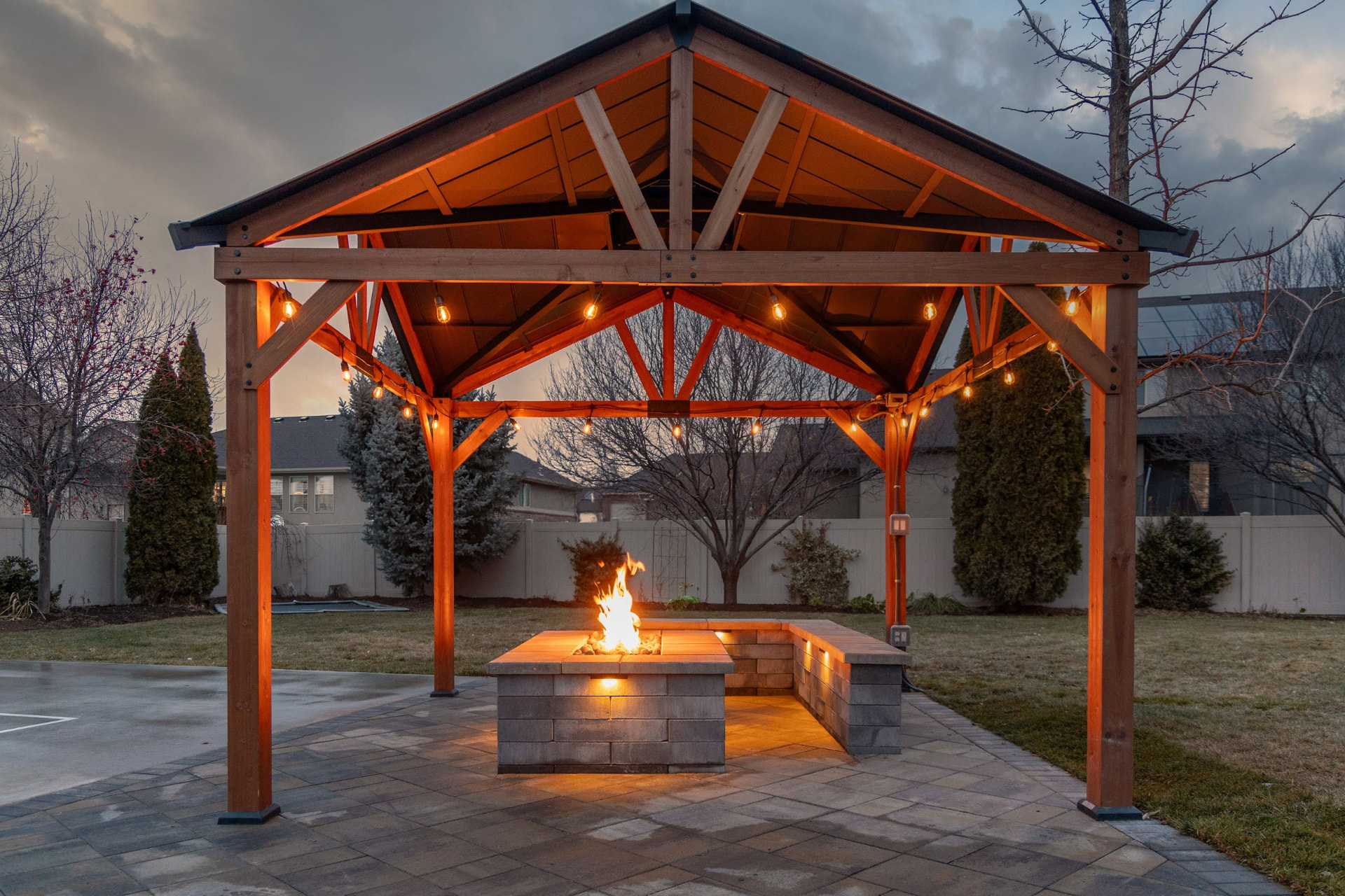 Covered pavilion with a stone outdoor kitchen lit at dusk