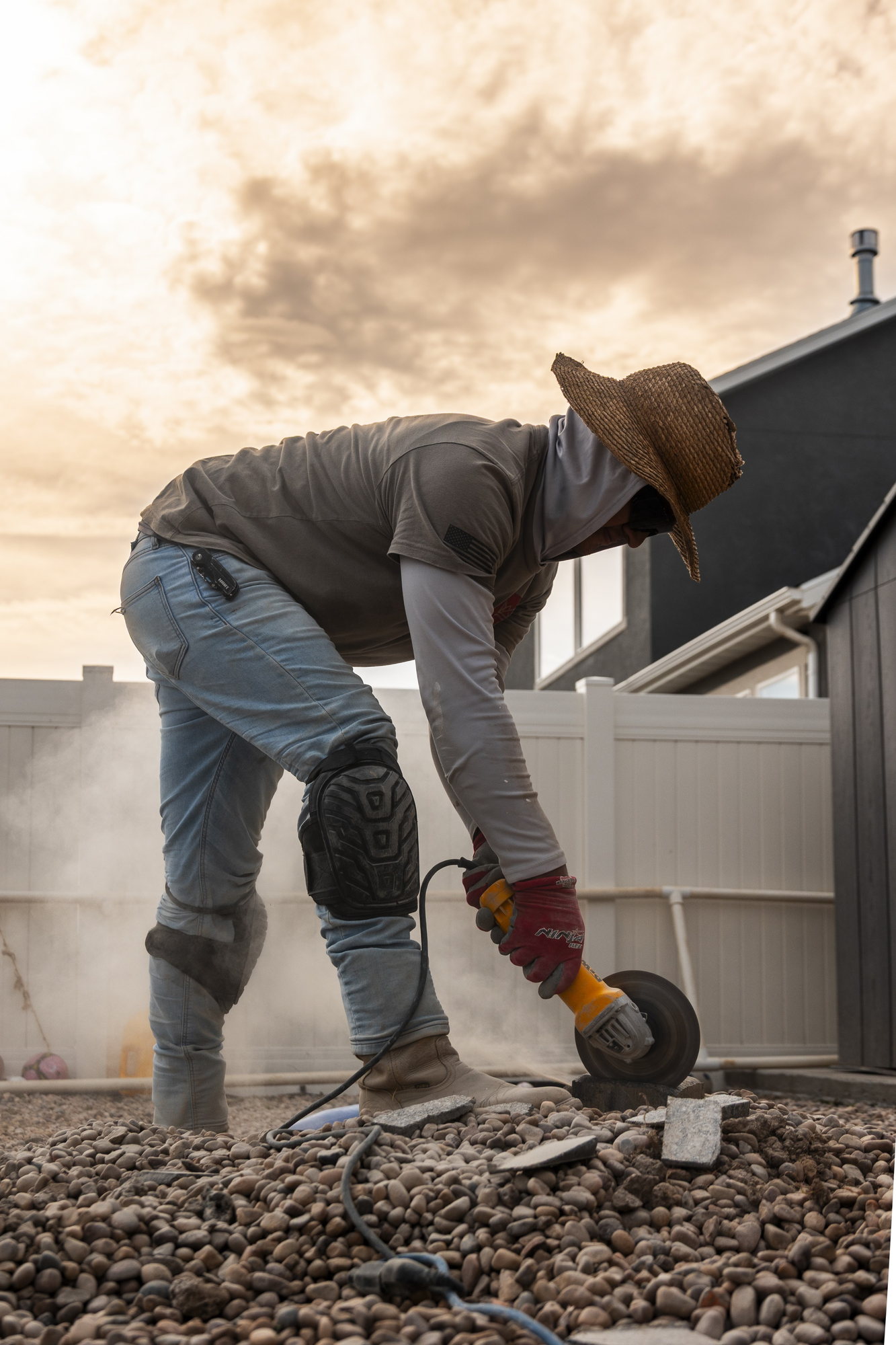 ULL crew member cutting a paver with an angle grinder, dust lit by the sun