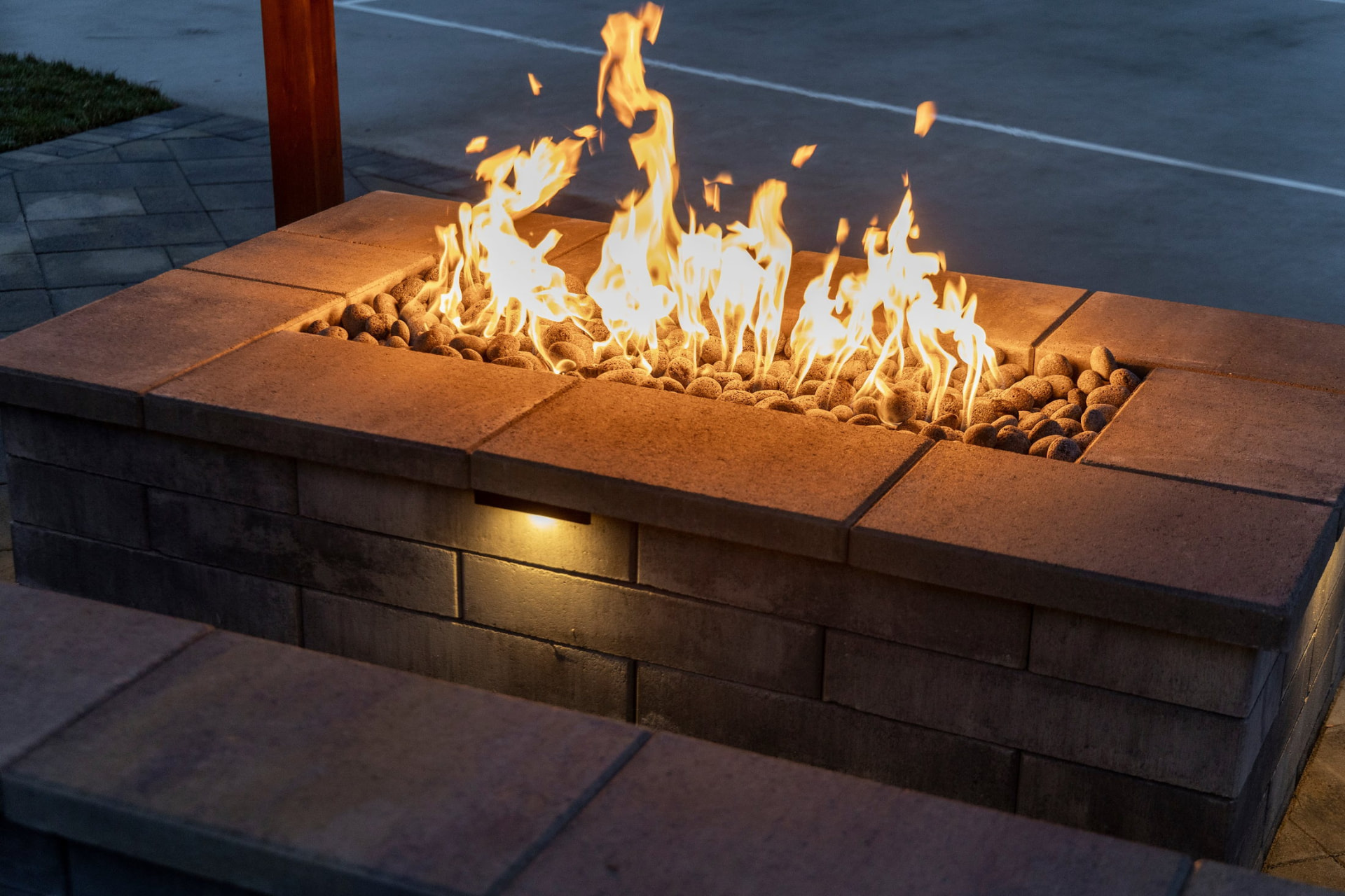 Close view of a lit fire table with wall lighting washing the block